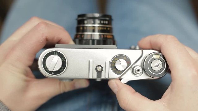 A young photographer changes settings of a vintage Soviet film camera, focuses and takes a picture. Close-up.
