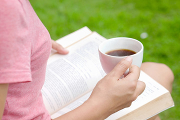 Woman holding a coffee mug reading a book in a park.