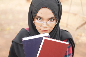 Portrait of happy young muslim woman black hijab and Scottish shirt holding a book in autumn season  background.