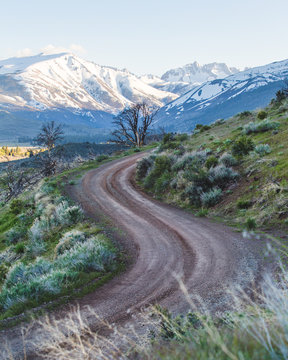 Curve in a dirt road with a snowy mountain backdrop during golden hour