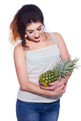 Summer studio portrait of a beautiful young brunette woman with long hair. A girl in a summer T-shirt and jeans is holding a pineapple in her hands. Concept: summer photography and a sunny mood