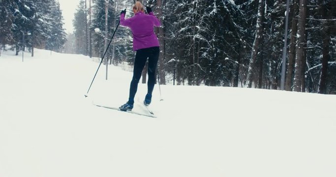 TRACKING Young adult Caucasian female athlete practicing cross-country skiing on a scenic forest trail. 4K UHD 60 FPS SLO MO