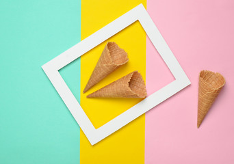 Two empty waffle horns in a white rectangular frame on a colored pastel background. Minimalist...