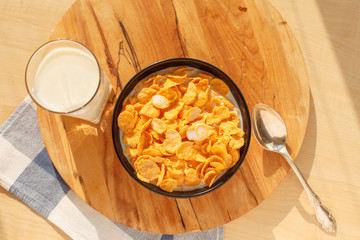 Cornflakes breakfast cereal in the bowl with glass of milk on wood table
