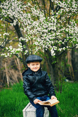 Boy in the spring flowering garden with a book in his hands