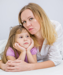 Woman hugs her sad daughter on the bed