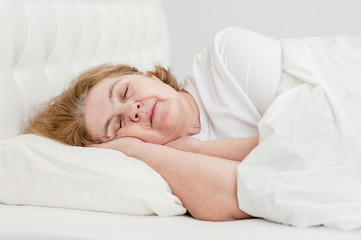 Tired senior woman sleeping on bed