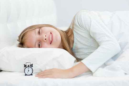 smiling girl lies on the bed with a clock