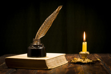 Education and writing concept, pen in ink bottle and candle holder with candle on wooden table.