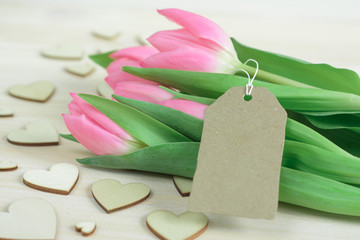 Spring desktop with pink tulips, craft lable and wooden hearts