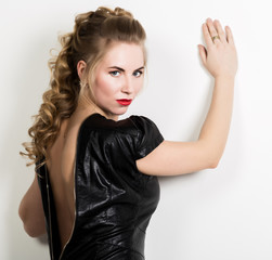 Beautiful young woman wearing short leather black dress with naked back on a light background