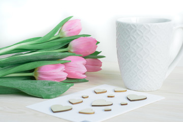 Tender desktop with pink tulips, ceramic mug and card with wooden hearts