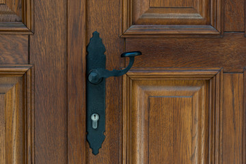 Black vintage metal door handle on brown wooden doors.