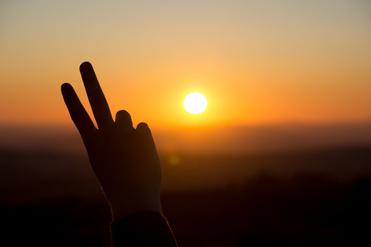 A peace sign hand gesture is silhouetted by the setting sun in Dartmoor, UK