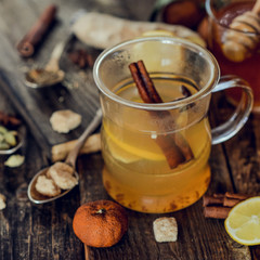 Vitamin healing tea with lemon and honey, ginger and spices on wooden background in rustic style. The concept of spring beriberi and colds. Square image.