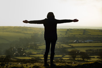 Fototapeta na wymiar A young woman looks over the moors of Liskeard, Cornwall, UK with her arms outstretched