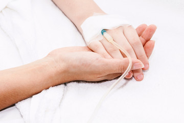 Mother holding little girl hand with IV saline intravenous in hospital