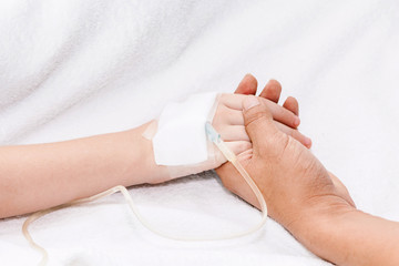 Mother holding little girl hand with IV saline intravenous in hospital