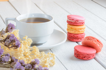 Different types color of macaroons with Cup of hot tea on white wooden background