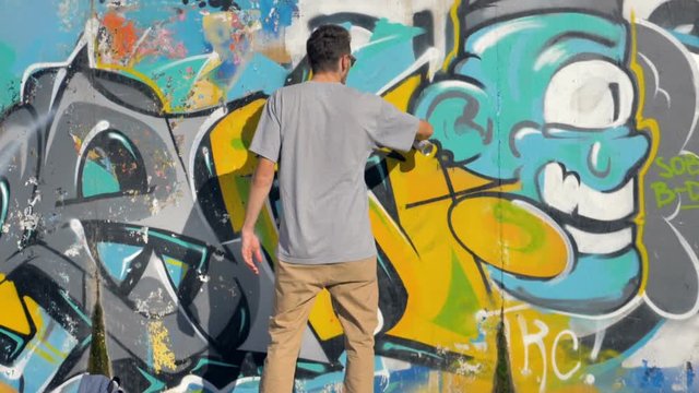 Artist is painting a yellow letter on the wall, view from behind.