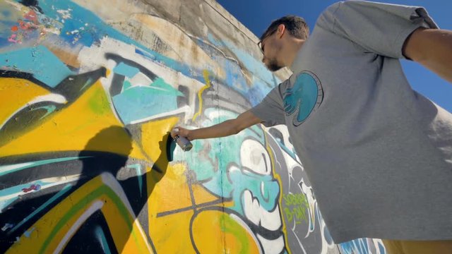 Graffiti artist is painting a yellow letter on the wall, view from left side, from below.