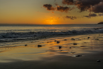 Sunset on the beach of Fuerteventura with lava rocks, dark clouds and small waves