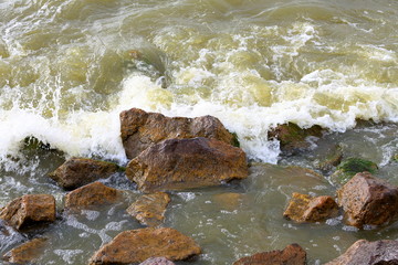 Stones in the murky muddy brown green shallow water of the lake surf