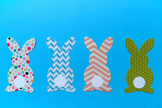 Easter bunny decoration on blue background, copy space. DIY holiday handicraft of colorful rabbits. Flat lay, top view. Border of paper rabbits cutouts. Easter greeting card. Happy Easter concept.