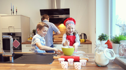Young father with two happy children backing cookies in modern kitchen