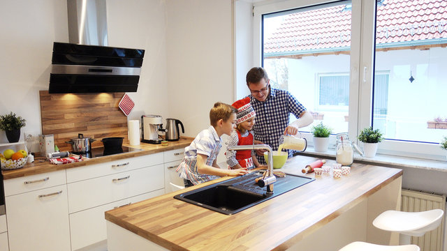 Young father with two happy children backing cookies in modern kitchen - Powered by Adobe