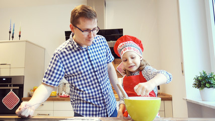 Young father with pretty little daughter backing cookies and having funat home