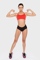 Fototapeta na wymiar A strong young woman demonstrates her hands muscles standing on a gray background