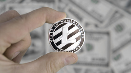 Litecoins crypto currency on US dollars in hand. Digital currency close-up. New virtual money. Real coins of Litecoins on banknotes of one hundred dollars. Bussiness, commercial.