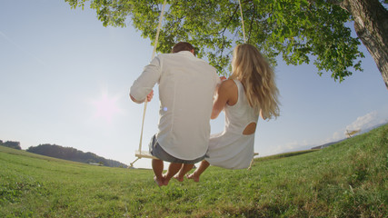 CLOSE UP: Teenage couple on a date swinging under tree on sunny day © helivideo