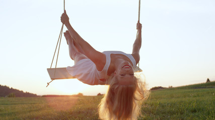LENS FLARE, CLOSE UP: Attractive young woman leans back on swing while swaying. - obrazy, fototapety, plakaty