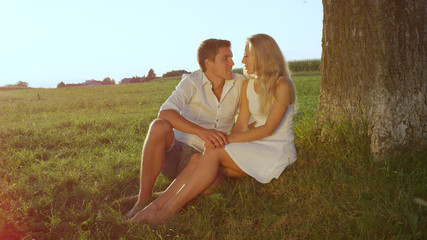 Fototapeta na wymiar LENSE FLARE: Embraced young couple sharing an intimate moment in a sunlit meadow
