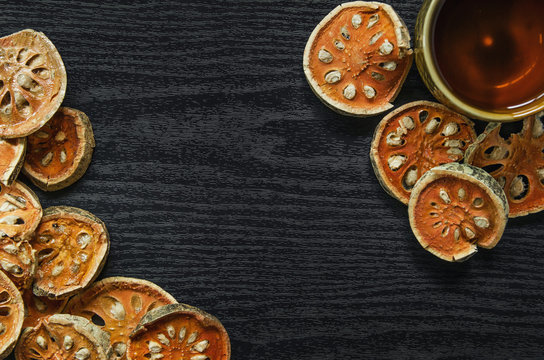 Dried herbs and dried bael fruit, Top view of bael dry and glass tea and bael juice on the wooden floor, Slices of bael fruit on the dark table. © Phanithi