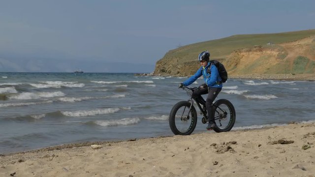 Fat bike also called fatbike or fat-tire bike in summer driving on the beach. The guy was riding a bicycle, then stopped and sat on the wheel of his bicycle. He looks at the sea and enjoys his sight.