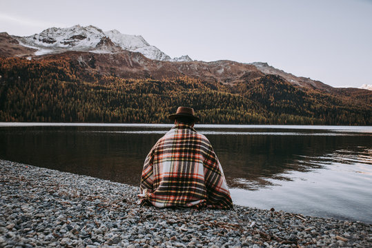 Lonely man enjoying sunrise on a lake beach with mountains background