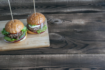 Two burgers on a wooden plate.