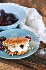 Round waffles with fresh blackberries and whipped cream, on natural wooden background in rustic style