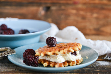 Round waffles with fresh blackberries and whipped cream, on natural wooden background in rustic style