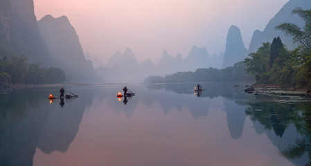 De Li-rivier, Xingping, China, toneellandschap. Aalscholvervissers op de oude bamboeboten met aangestoken lampen bij zonsopgang.