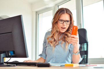 Furious businesswoman wearing suit working on line using a smart phone in a desk at office