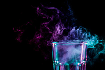 Close up of a new glass with soft multi-colored purple and green smoke from vape on a black isolated background