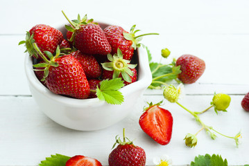 fresh ripe and under ripe strawberry fruits, flowers, leaves on white wood table background