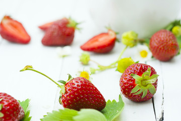 fresh ripe and under ripe strawberry fruits, flowers, leaves on white wood table background