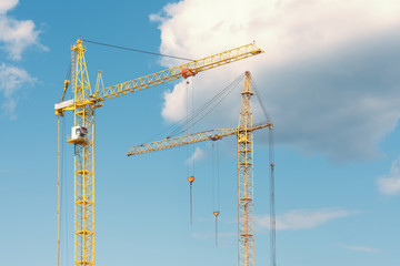 Two yellow cranes against the blue sky and clouds