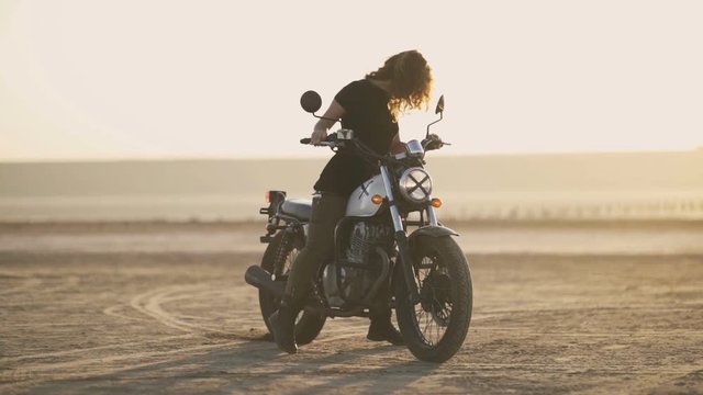 beautiful young woman riding on an old motorcycle and doing a trick. in the desert at sunset or sunrise. Female biker. Stabilized shot 