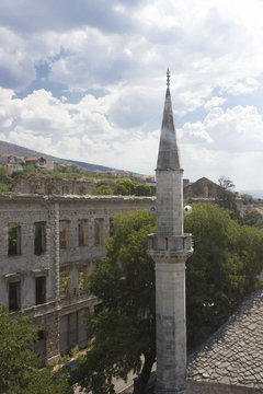 Minaret tower in Mostar city, with a ruined building on its side